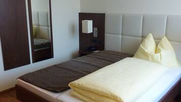 A neatly made bed with a white mattress and a brown headboard. There is a large mirror on the wall to the left of the bed.