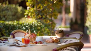 Mesa al aire libre con alimentos para el desayuno, como pan, una taza y un vaso de jugo.