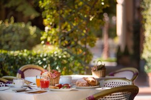 Une table dressée à l’extérieur, avec des aliments pour le petit-déjeuner, notamment du pain, une tasse et un verre de jus.