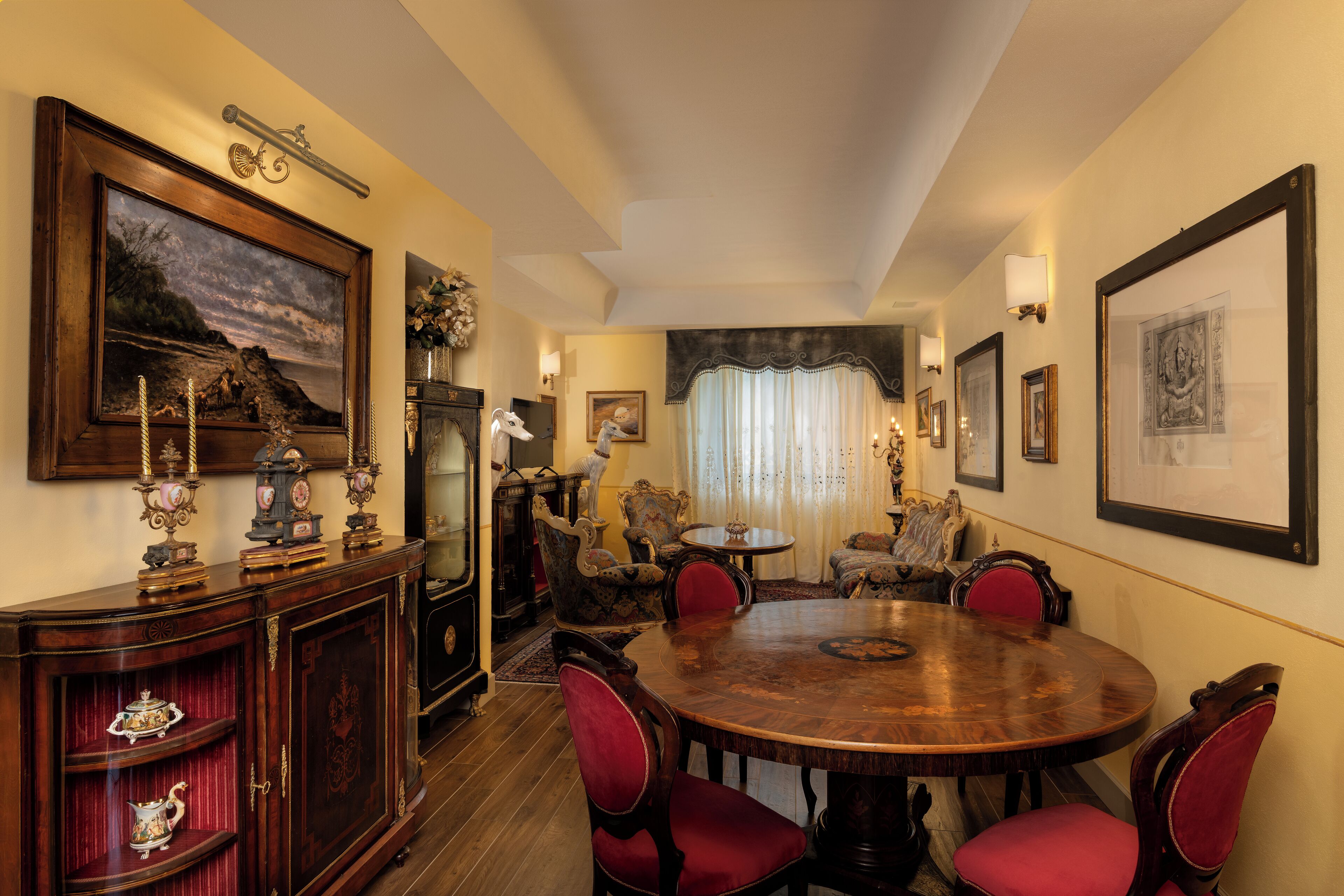 Uma sala de jantar com uma mesa de madeira redonda, cadeiras estofadas vermelhas e um aparador antigo com objetos decorativos.