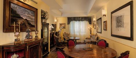 A dining area with a round wooden table, red upholstered chairs, and a vintage cabinet with decorative items.