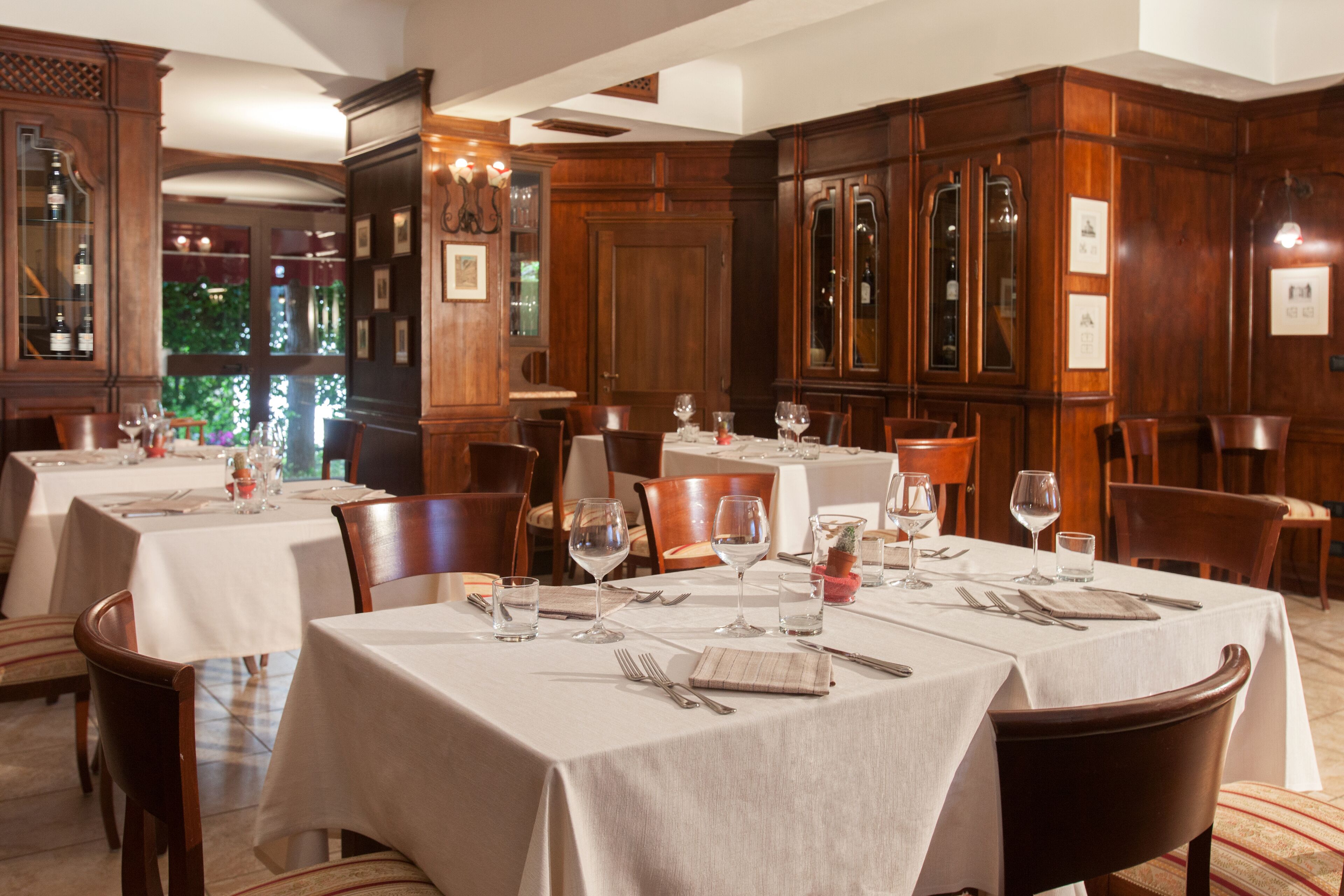 Une salle à manger avec plusieurs tables dressées pour le service, des panneaux de bois et des tableaux encadrés aux murs.