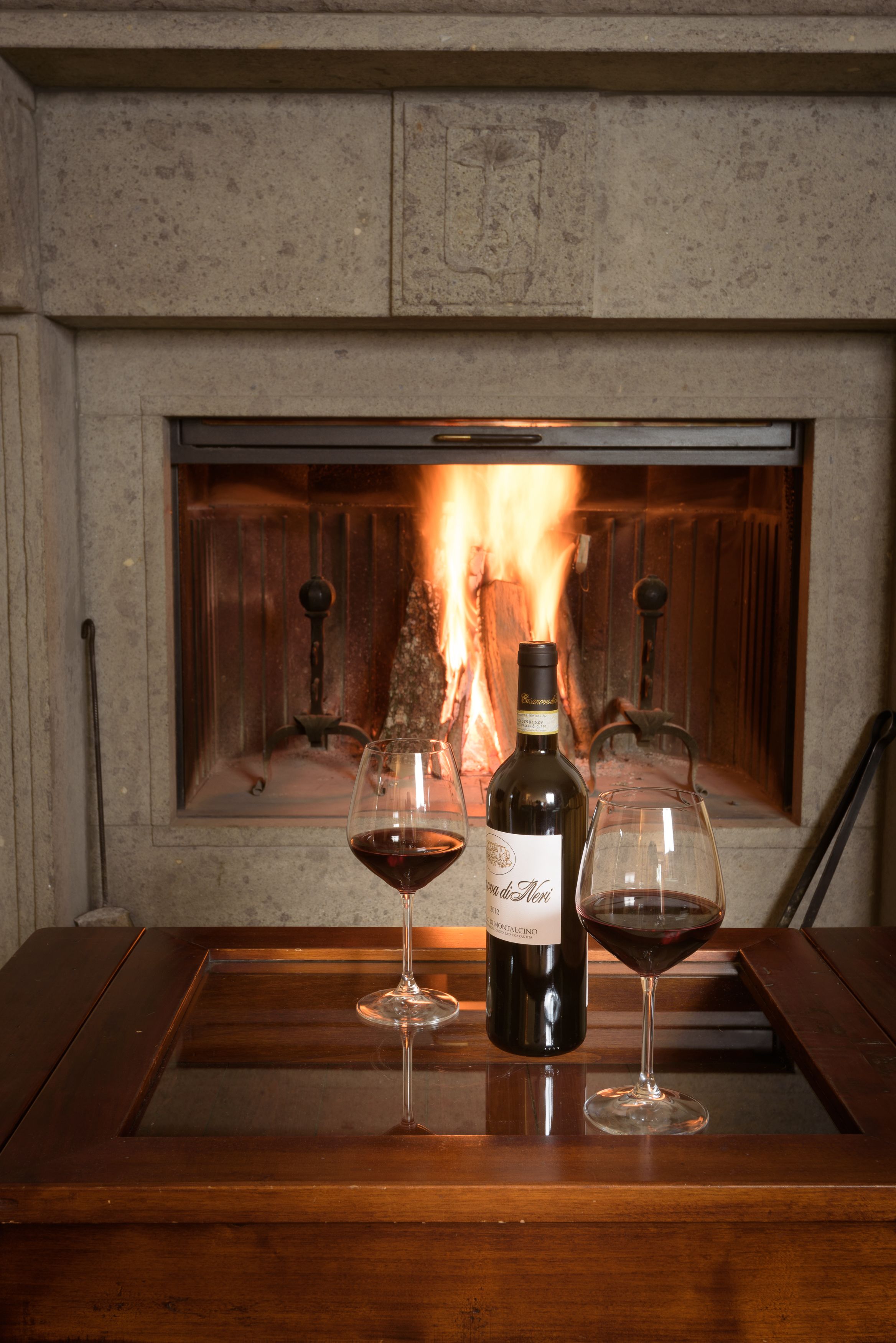 A fireplace with a bottle of wine and two wine glasses on a wooden table.