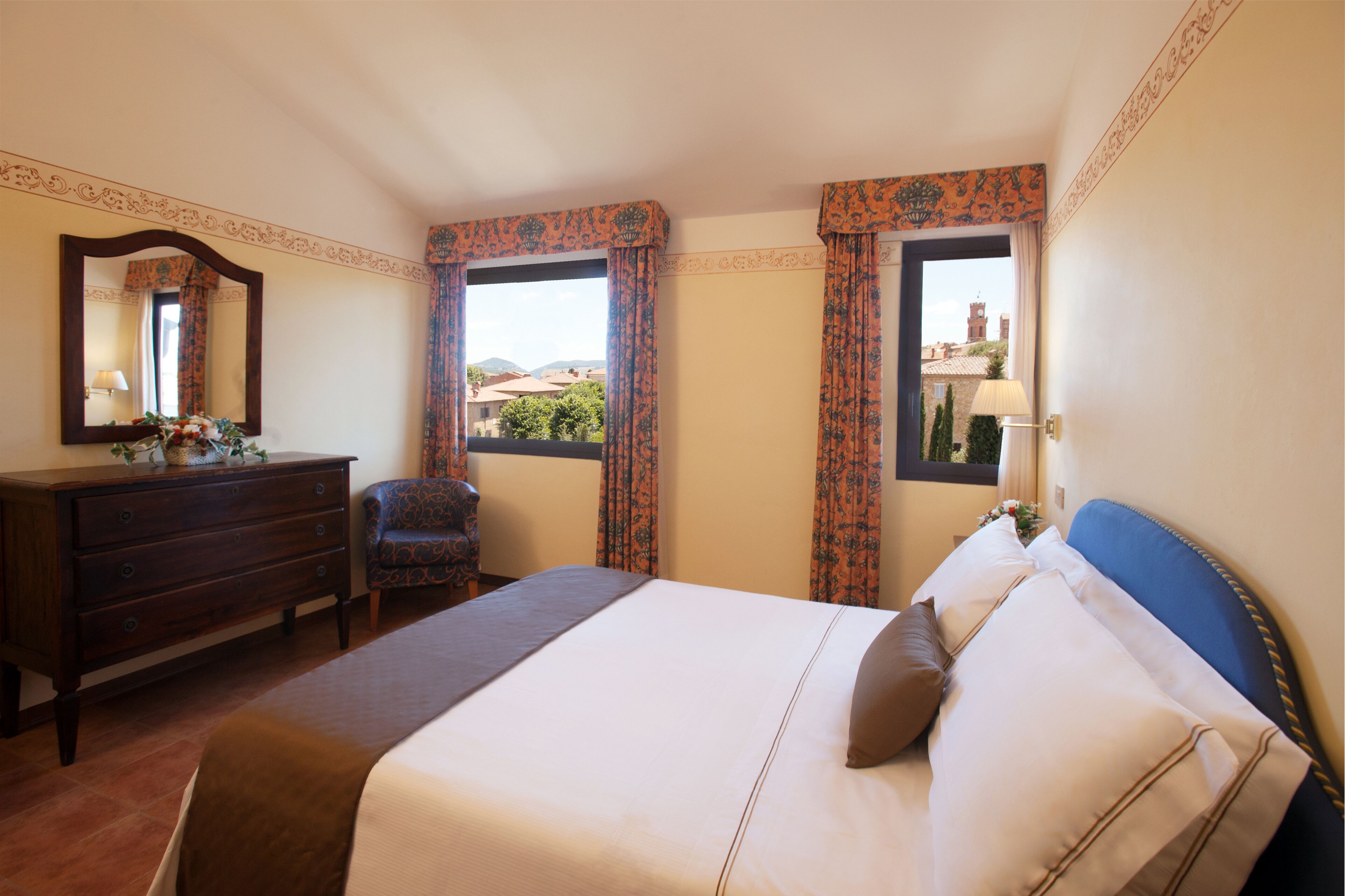 A hotel room with a bed, dresser, chair, and windows with curtains.