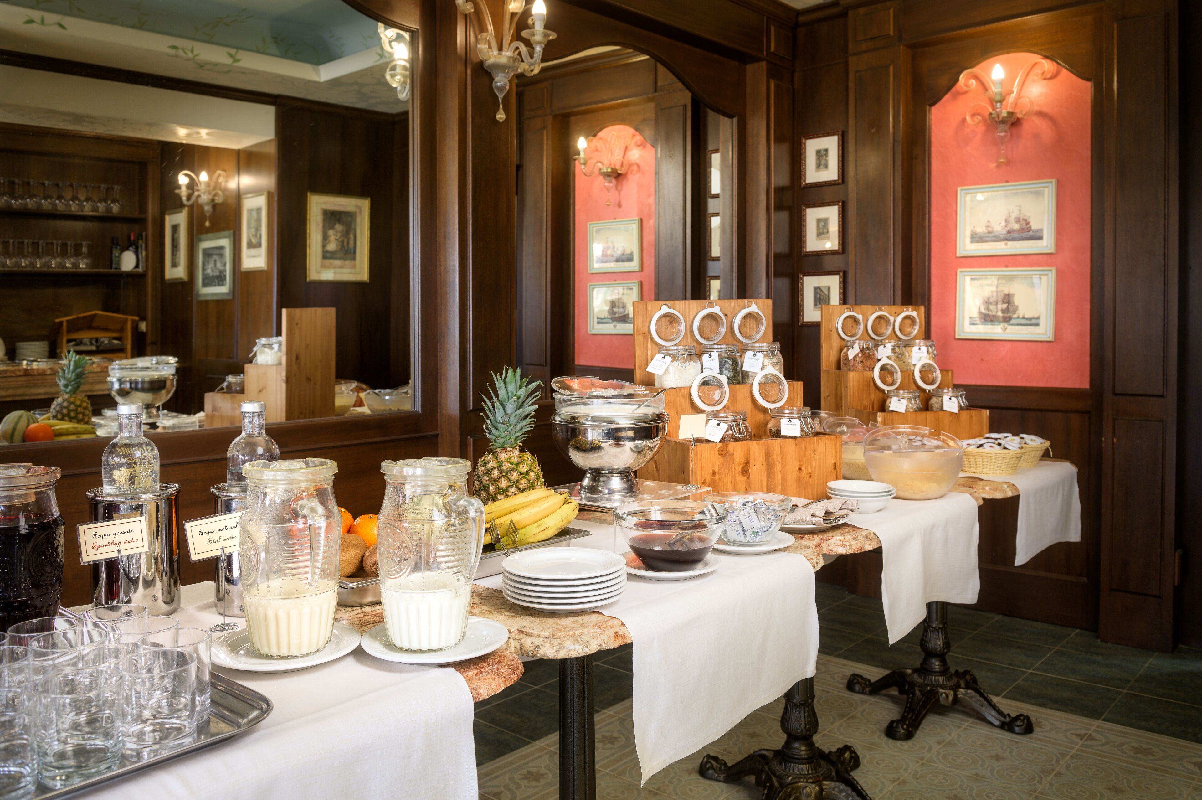 A buffet setup with various food items and beverages, including jars of condiments, a fruit bowl, and a variety of dishes on a marble table.