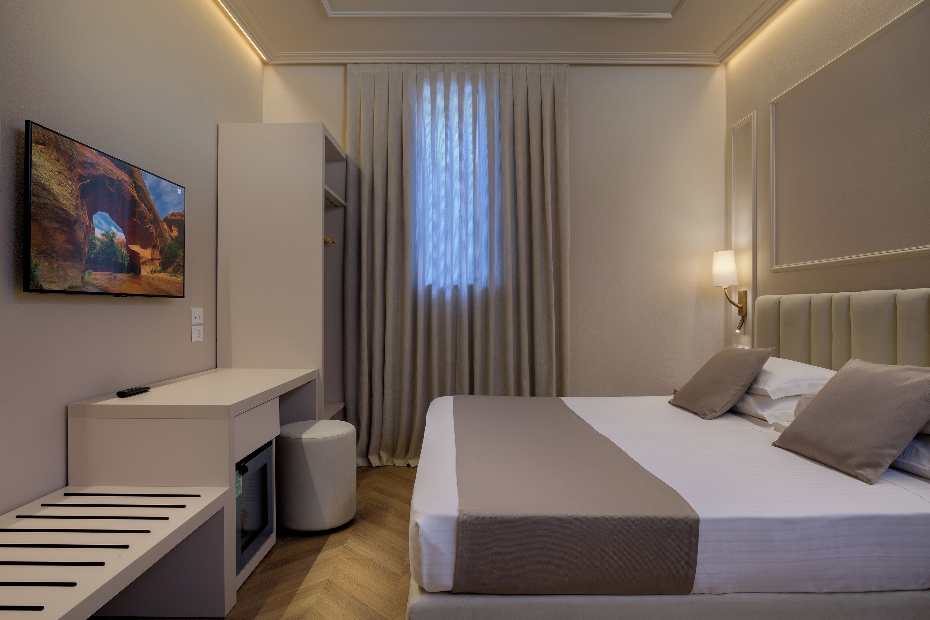 A hotel room with a bed, a desk, a television, and a window with curtains.