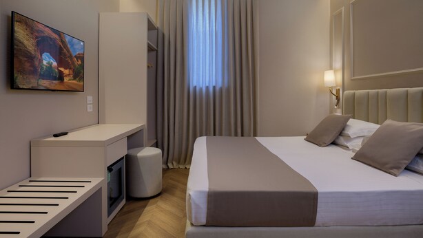 Habitación de hotel con una cama, un escritorio, un televisor y una ventana con cortinas.