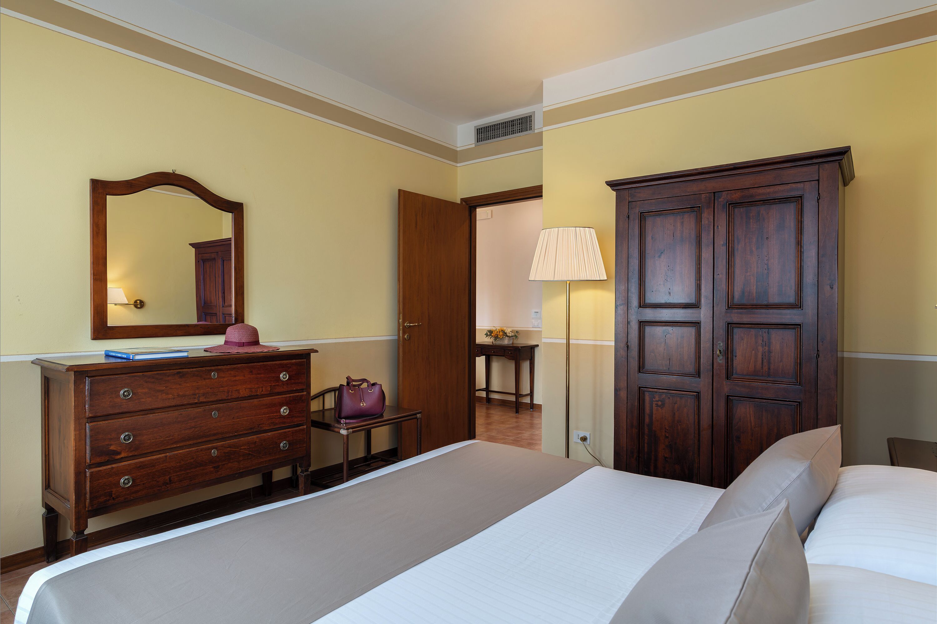 A hotel room with a bed, dresser, mirror, wardrobe, and a lamp.