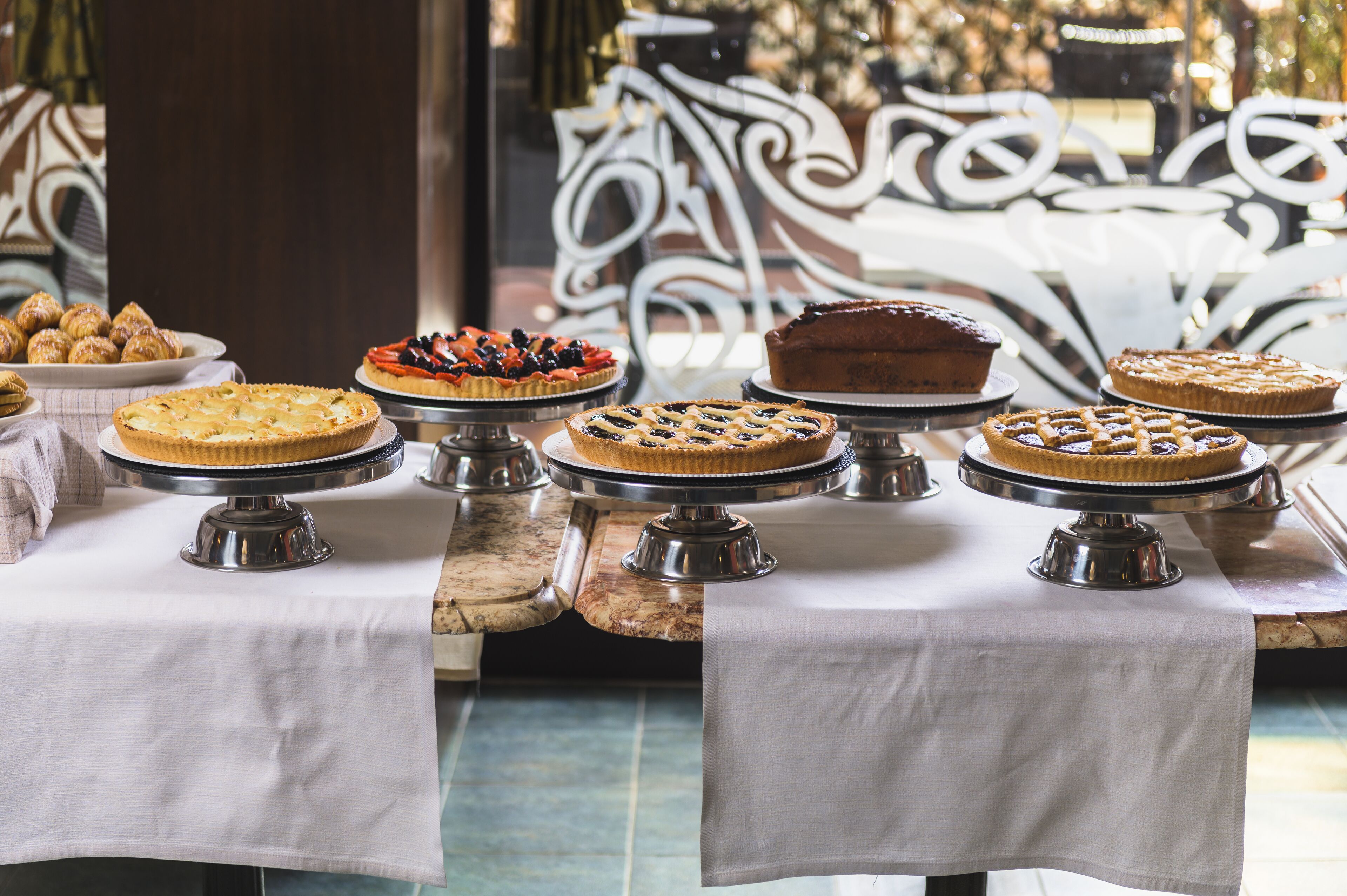 Una mesa con varios pasteles y postres sobre soportes metálicos, colocada sobre una tela blanca.