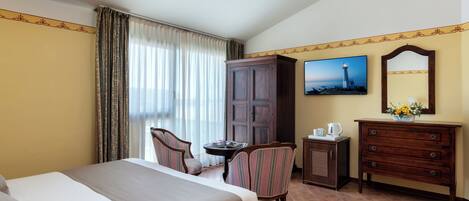 Quarto de hotel com cama, escrivaninha, cadeira, cômoda, televisão e janela com cortinas.