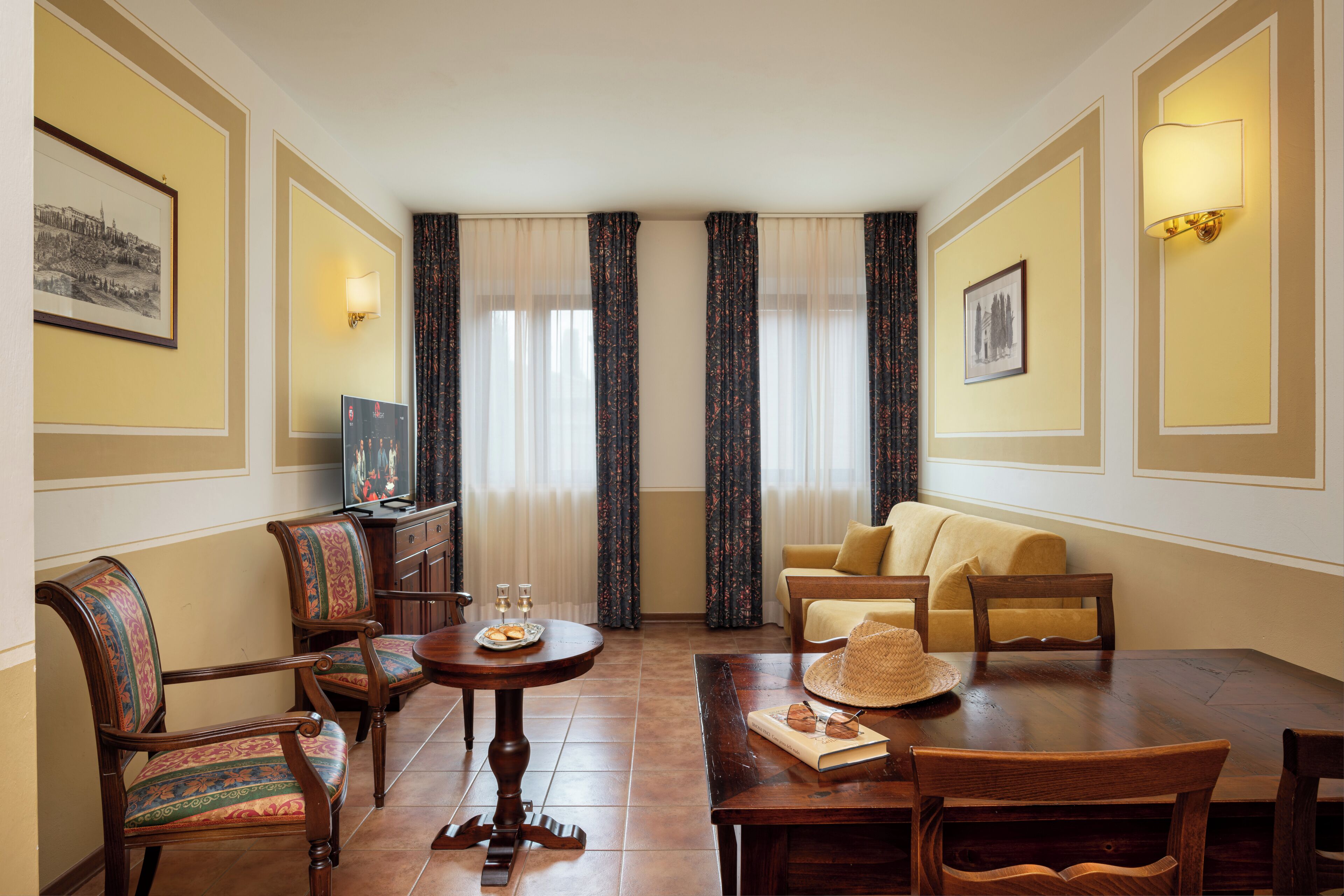 A hotel room with a dining table, chairs, a sofa, and a TV.