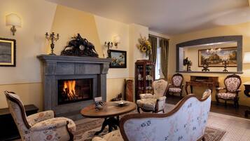 Un salon traditionnel avec une cheminée, des fauteuils à motifs floraux, une table ronde en bois et une bibliothèque.