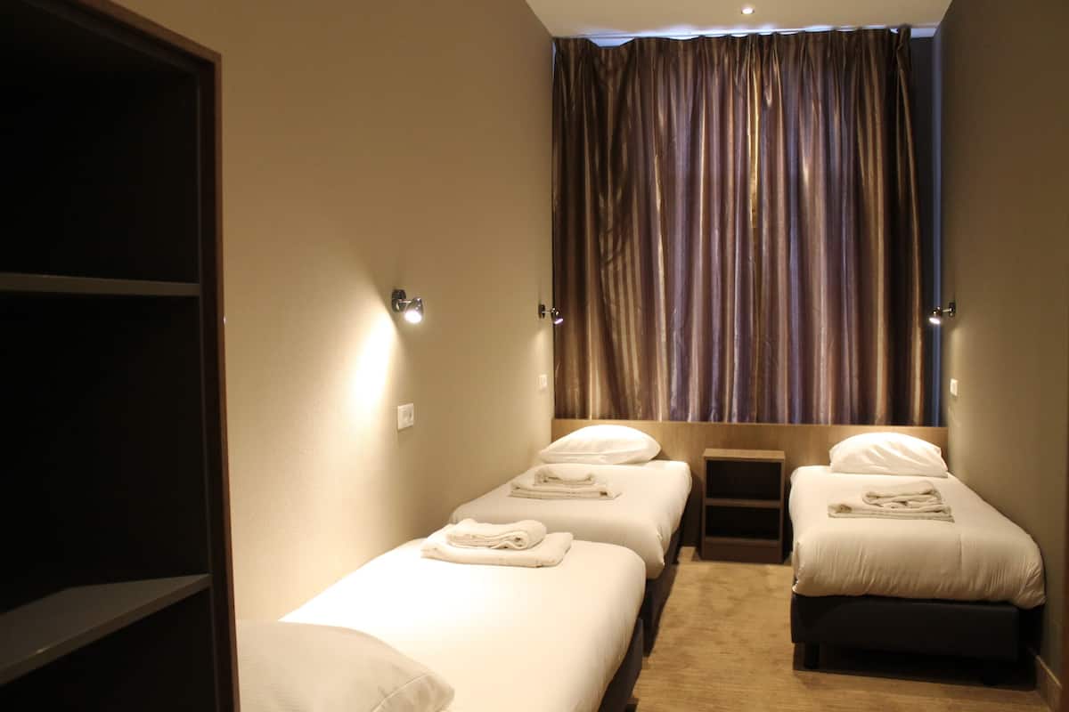 A hotel room with two single beds, a wardrobe, and a curtain.