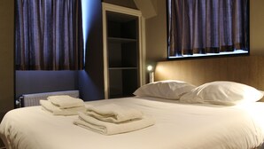 A neatly made bed with folded towels, a wooden headboard, and a window with curtains.