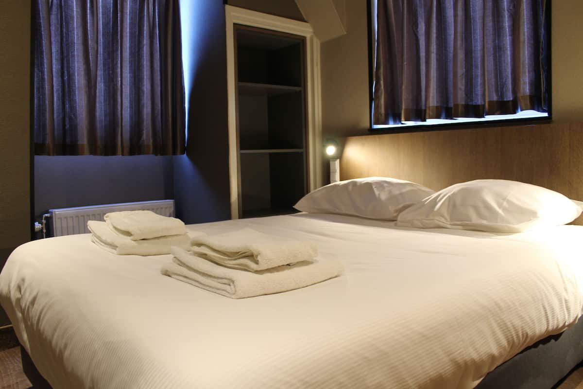 A neatly made bed with folded towels, a wooden headboard, and a window with curtains.