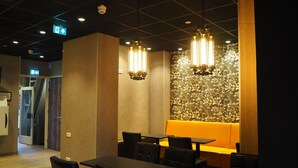 A modern dining area with a long table and chairs, a decorative wall with a floral pattern, and pendant lighting.