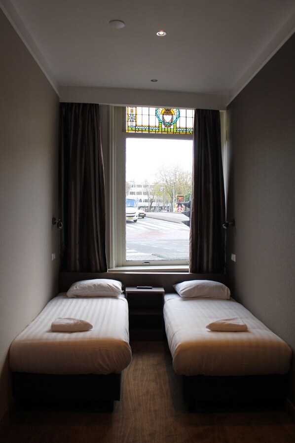 Habitación de hotel con dos camas individuales, una ventana con cortinas y vista a la calle.