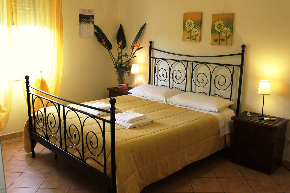 A neatly made bed with a yellow bedspread, a black metal headboard, and two bedside lamps.