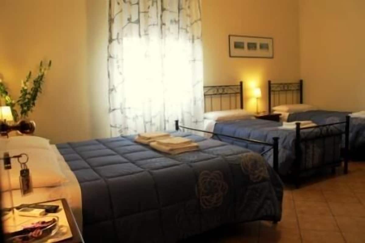 A hotel room with two beds, a desk with a lamp, and a window with curtains.