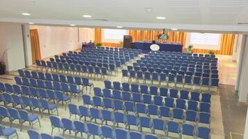 Une salle de conférence avec des rangées de chaises bleues, un pupitre et un écran de présentation.