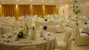 A banquet hall with round tables covered in white tablecloths, each set with plates, cutlery, and candles. The room has a high ceiling with recessed lighting and a golden curtain backdrop. - Centrum Palace (Campobasso)