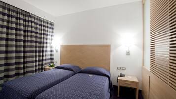 Una camera d'albergo con un letto grande, due comodini, una testiera in legno, un tavolino con il telefono e una finestra con tende.