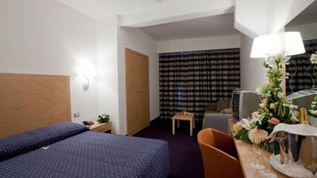 Ein Hotelzimmer mit Bett, Schreibtisch mit Lampe, Stuhl, kleinem Tisch und einem Fenster mit Vorhängen.