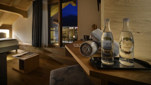 A wooden table with two bottles of Acqua di Livigno water, a rolled towel, and a black object on a tray. - Hotel Galli's - Centro (Livigno)