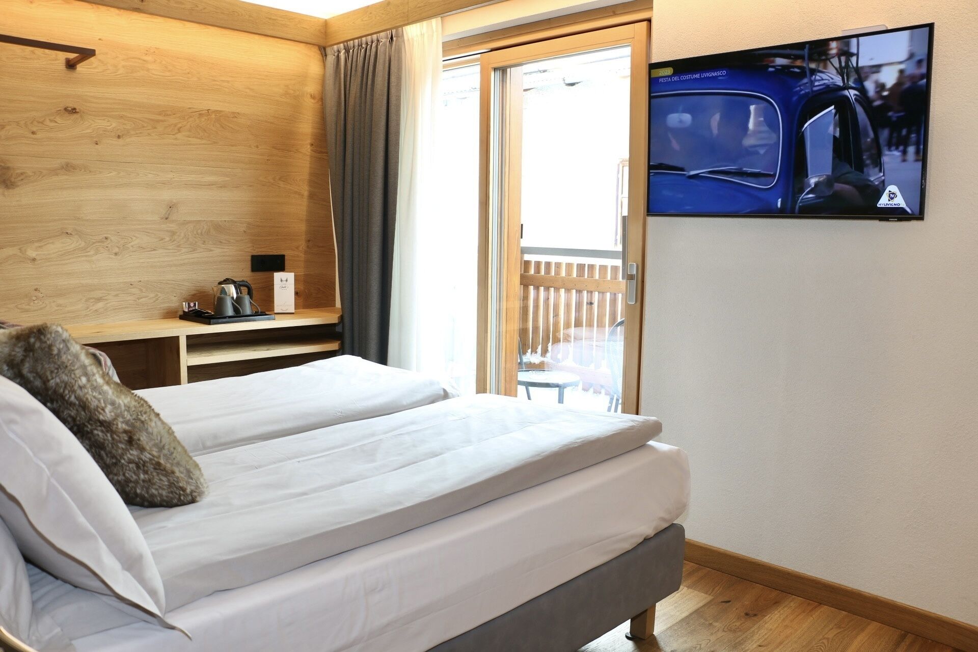 A hotel room with a bed, a TV mounted on the wall, and a wooden ceiling.
