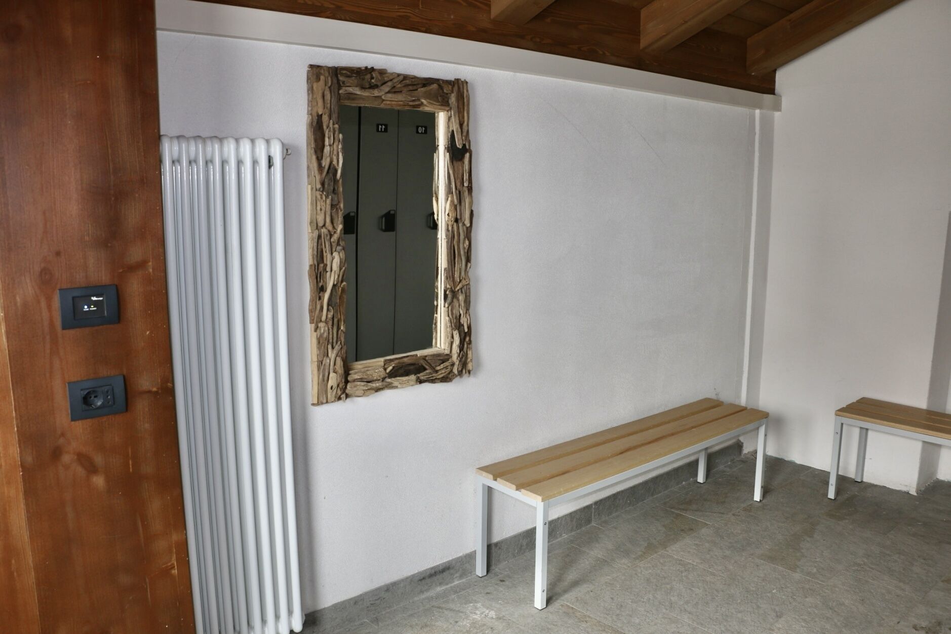 A room with a wooden bench, a radiator, and a mirror with a rustic frame.