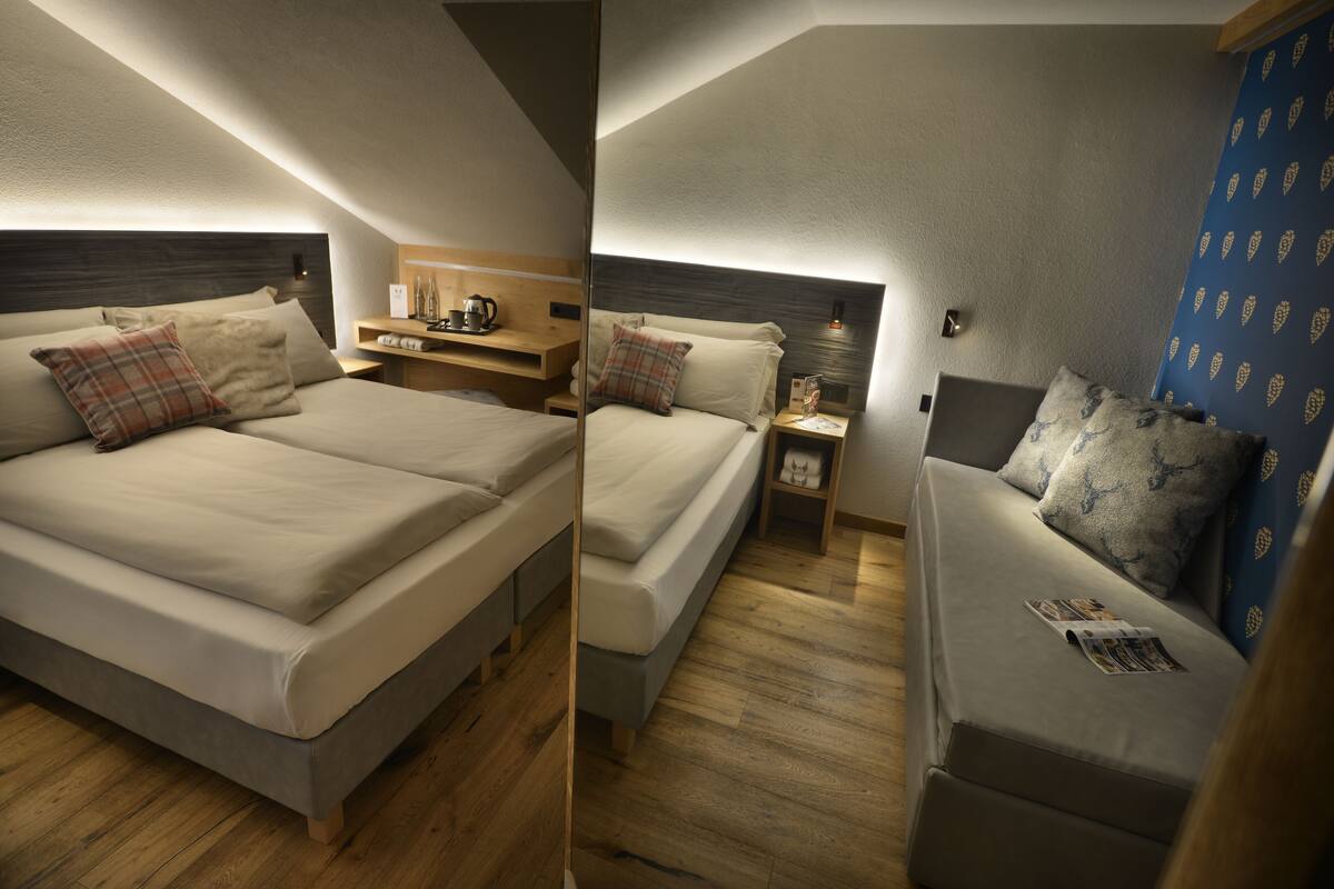 A modern hotel room with two beds, a wooden nightstand, a small table with a kettle, and a blue patterned wall.