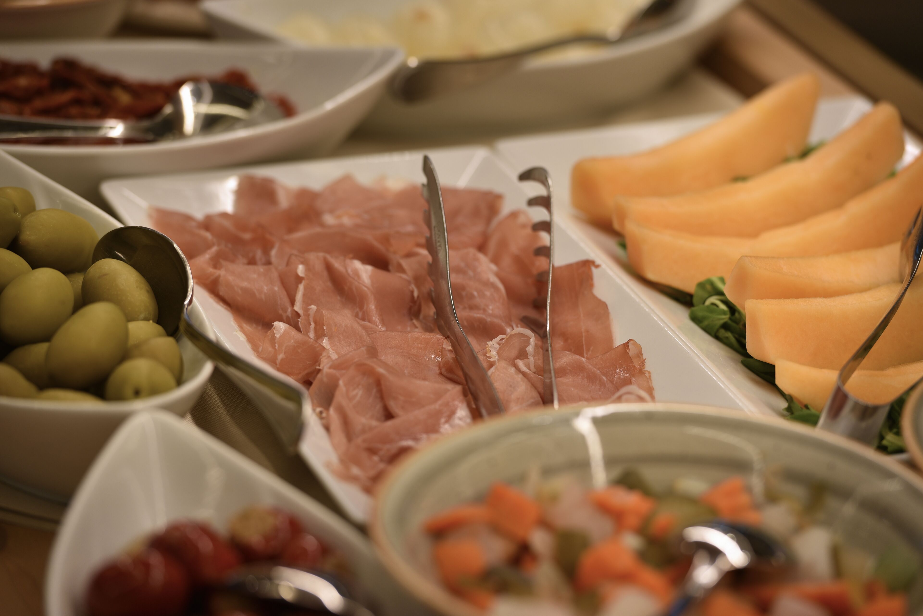 Un bufé con diversos alimentos, incluyendo aceitunas, carne en lonchas y verduras.