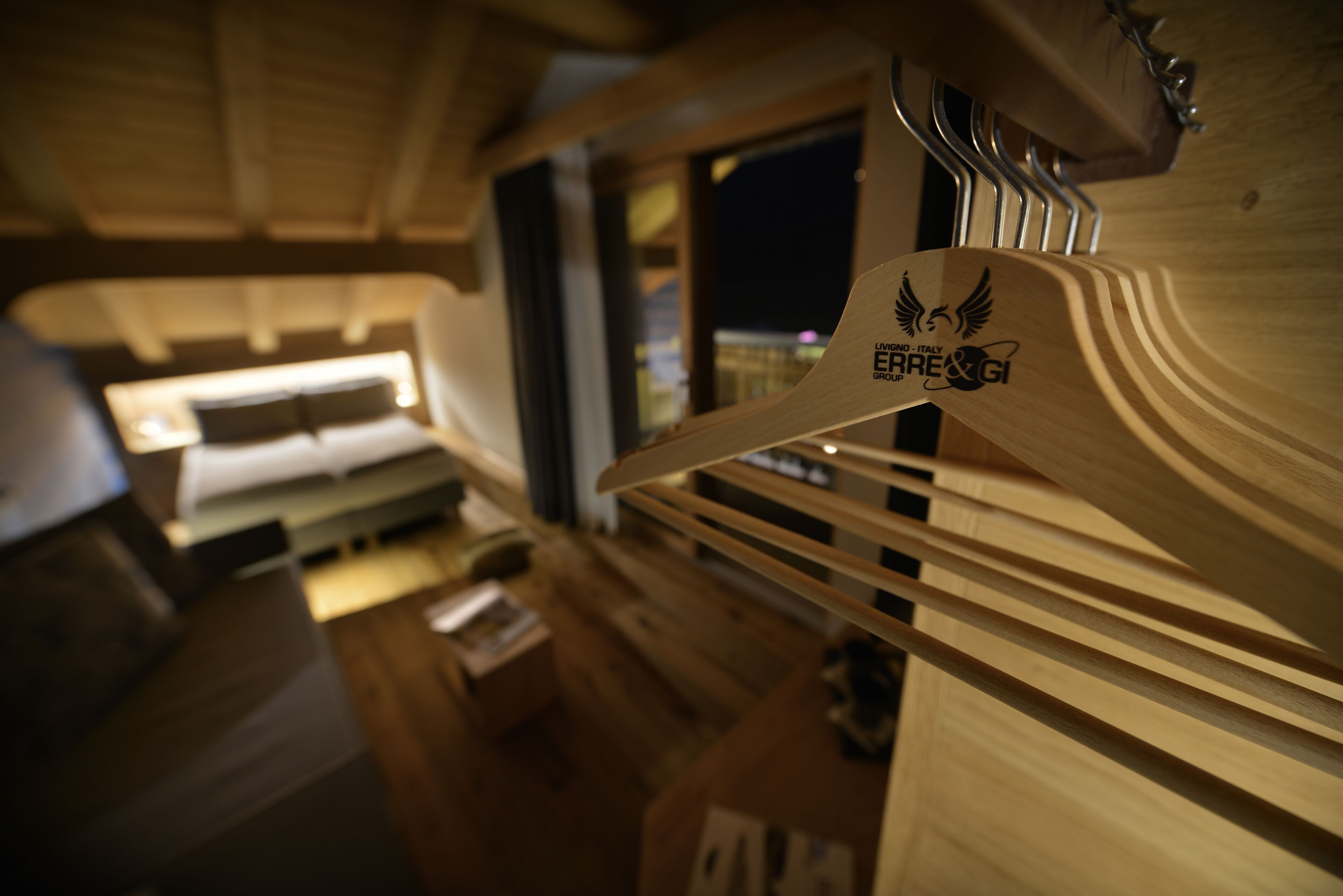 A wooden interior with a bed, a hanging wooden hanger with a logo, and a window with a view of the city at night.