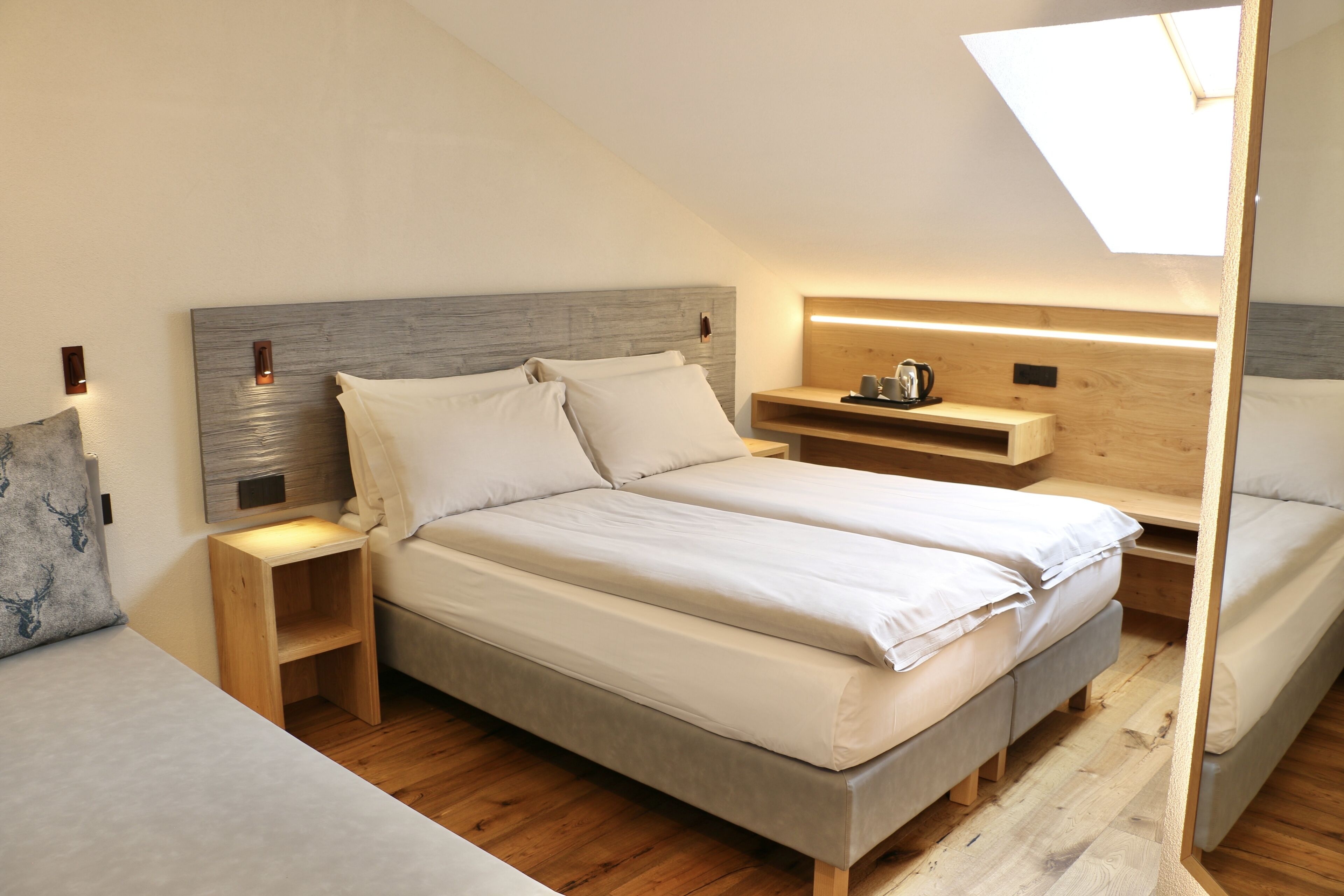 A modern bedroom with a large bed, wooden headboard, bedside tables, and a skylight.