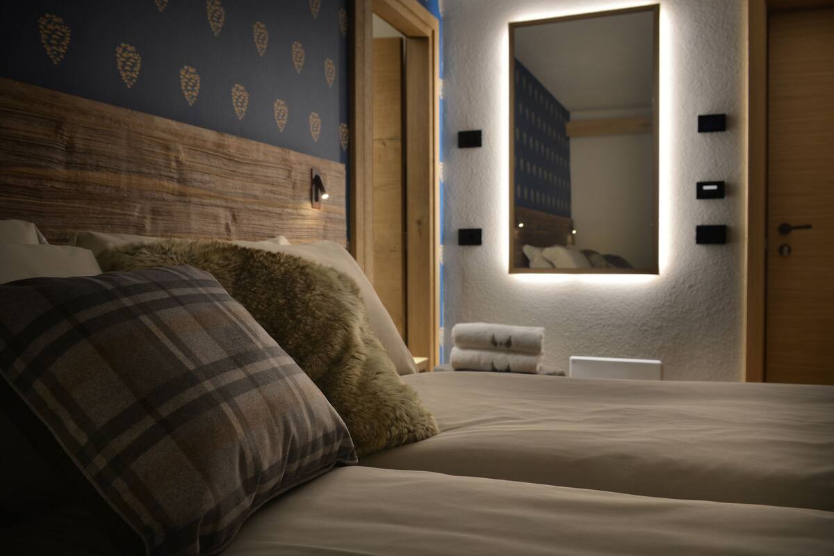 A bedroom with a large bed, two pillows, a nightstand, and a mirror.