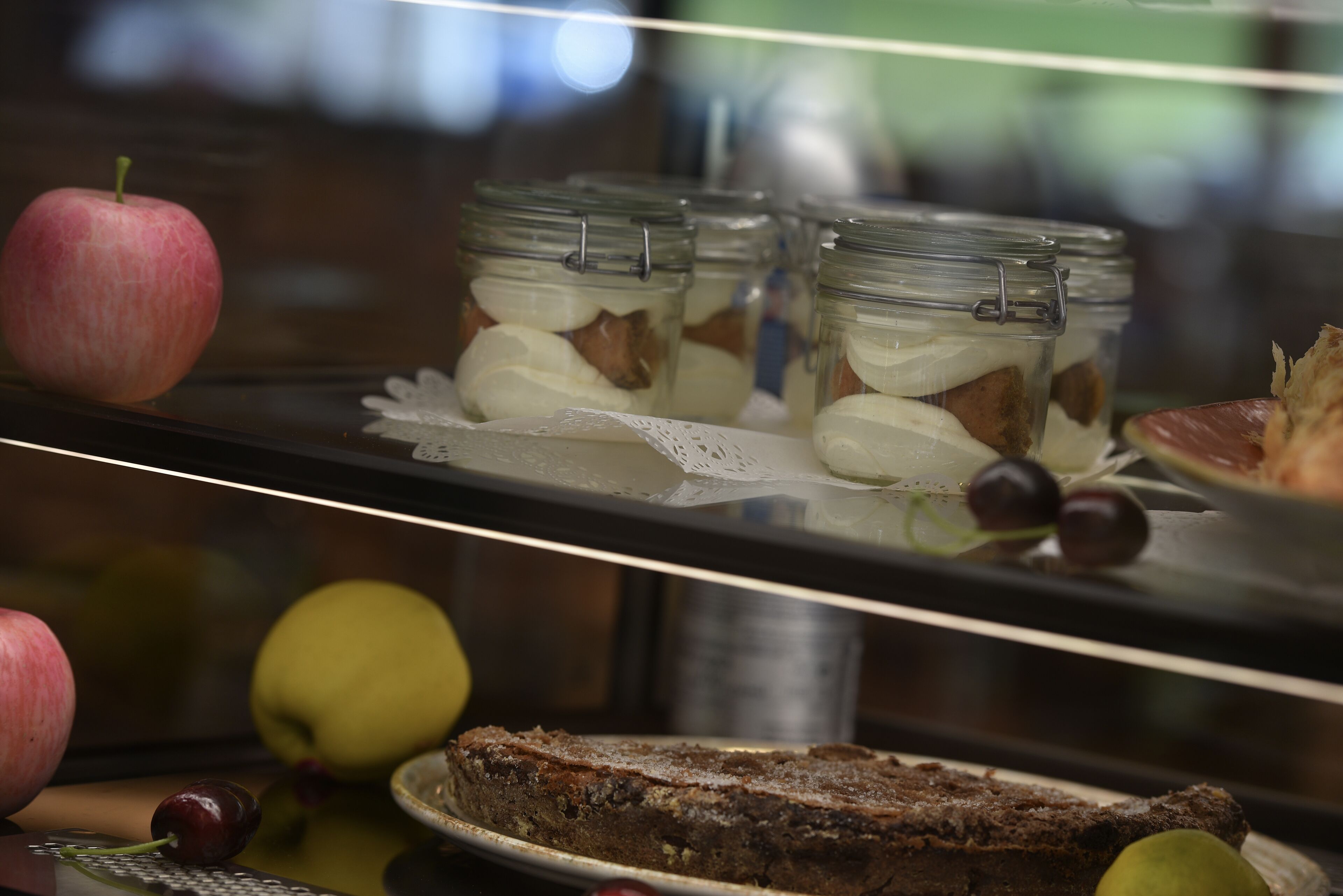 A display case with jars containing a dessert, a cake, and various fruits.