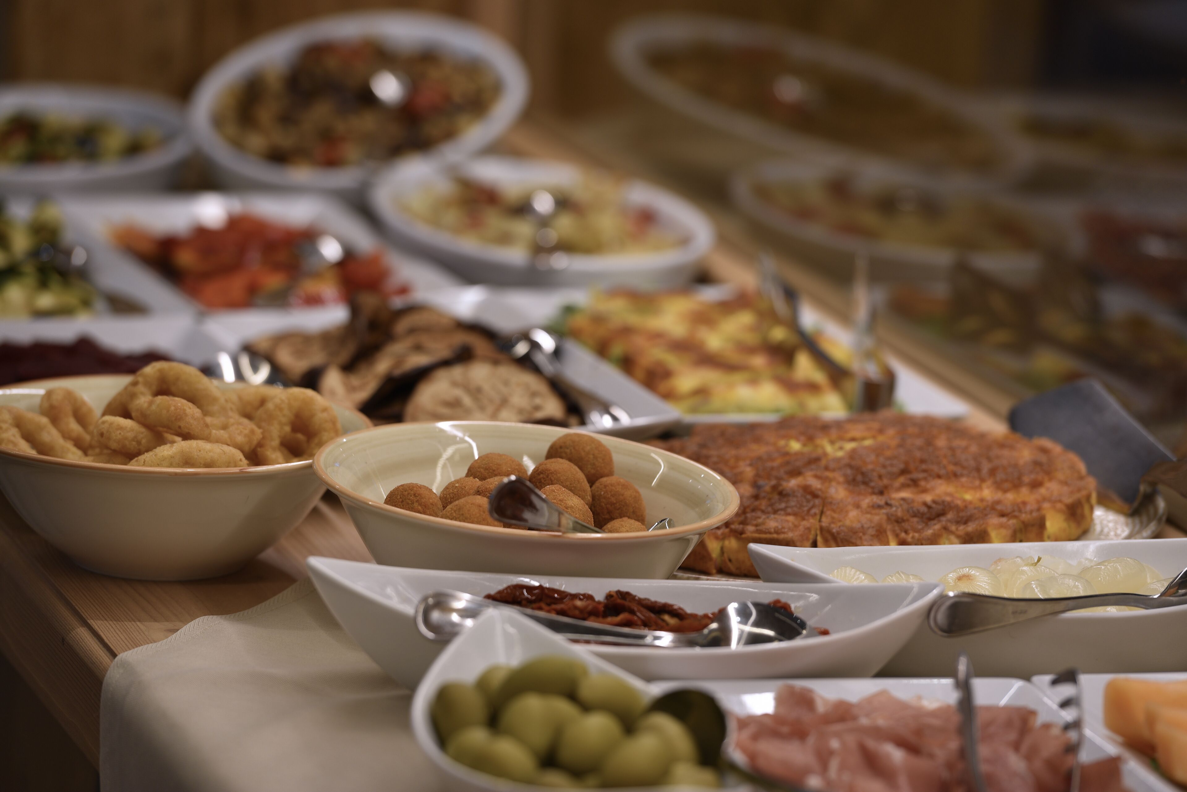 A buffet with various dishes including bread, olives, and a large omelette.