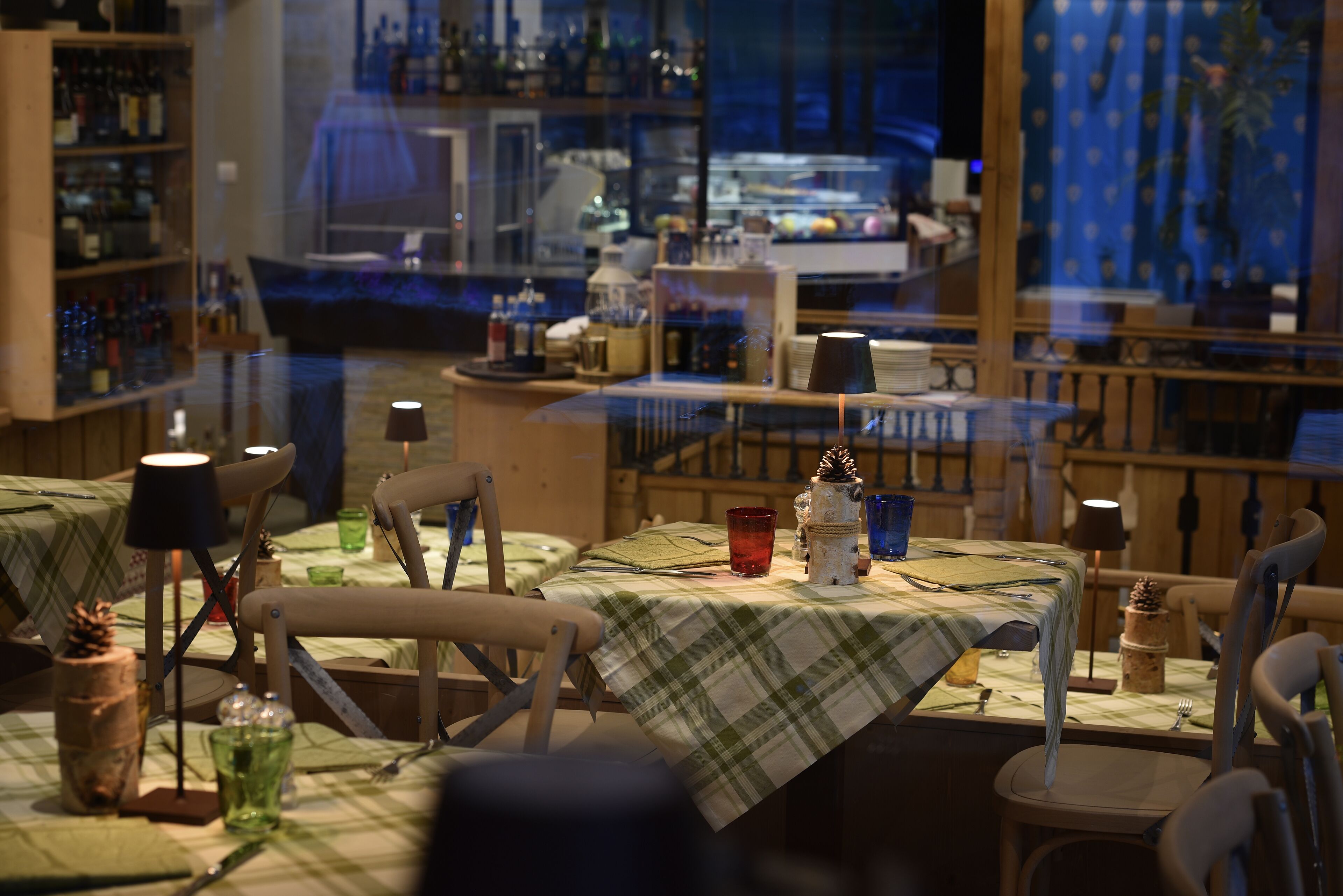 A cozy restaurant with wooden furniture and a view of the city through large windows.