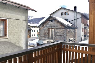 Un edificio de madera con tejado nevado, junto a un edificio moderno con balcón.