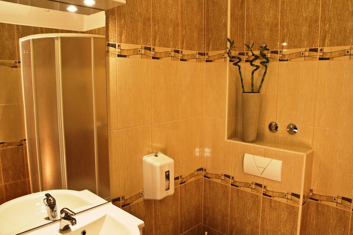 A bathroom with a sink, mirror, towel dispenser, and a shower area with a tub.