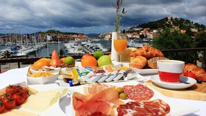 A table with a variety of food items and a view of a marina with boats and buildings. - Villa Diana (Tribunj)