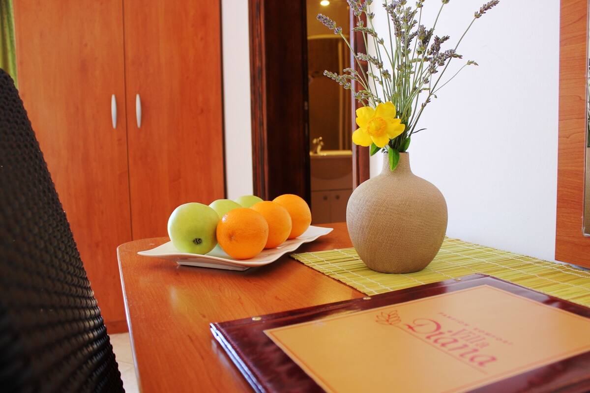 A wooden table with a vase of flowers and a plate of fruit.