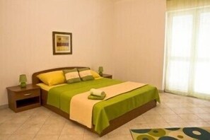 A bedroom with a bed, nightstands, a green and beige bedspread, a framed picture on the wall, and a window with blinds.