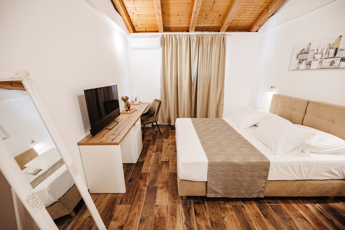 A bedroom with a wooden ceiling, a bed with white bedding, a desk with a computer, and a window with curtains.