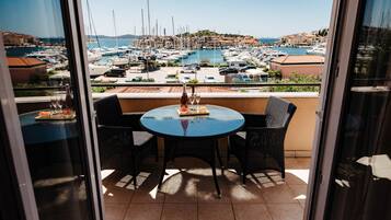 Ein Balkon mit einem runden Tisch und Stühlen, mit Blick auf einen Yachthafen mit Booten und Gebäuden.