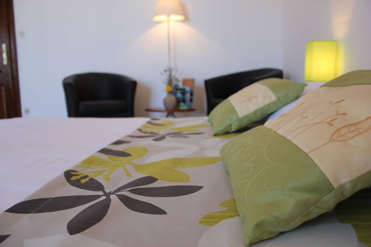 A hotel room with a bed, two chairs, a nightstand, and a lamp.