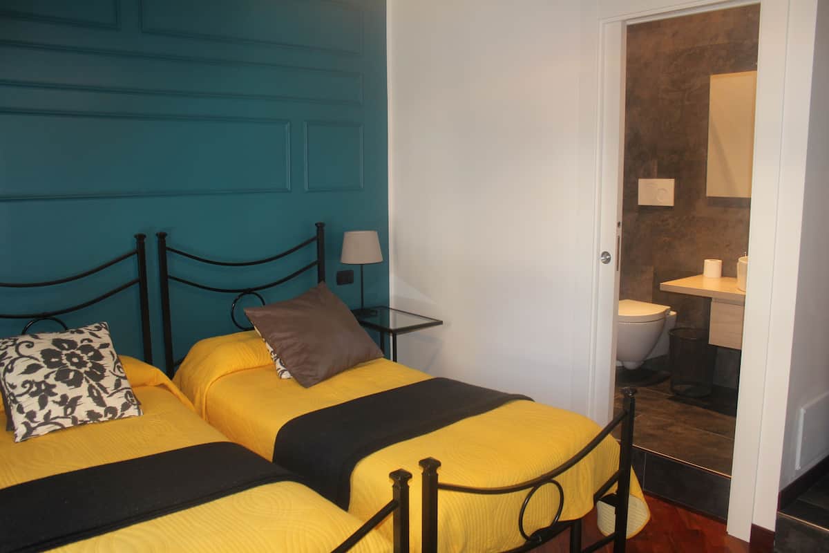 A room with two beds, a bathroom visible through an open door, and a blue wall.