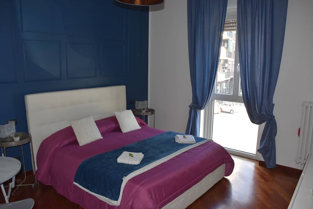 A bedroom with a large bed, a small table, and a window with curtains.