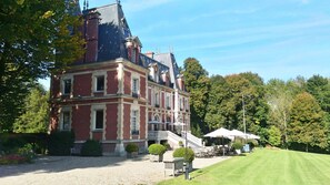 Un grand bâtiment à plusieurs étages, doté d’un escalier imposant menant à l’entrée, et entouré d’une pelouse bien entretenue et d’arbres.