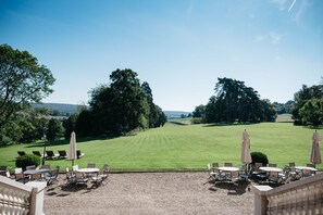 Un espace extérieur aménagé avec des tables et des chaises, donnant sur une pelouse bien entretenue et des arbres.